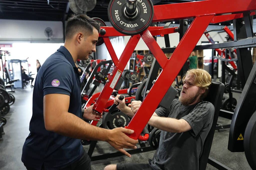 Personal trainer helping a client with weightlifting in a gym.