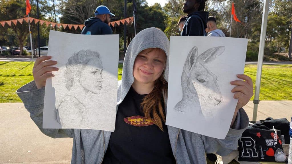 A young artist holding two sketches, one of a woman and another of a deer.