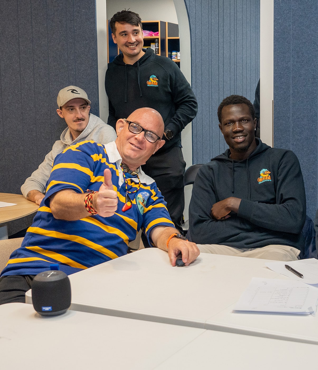 A group of four individuals enjoying a team meeting with one person giving a thumbs up.