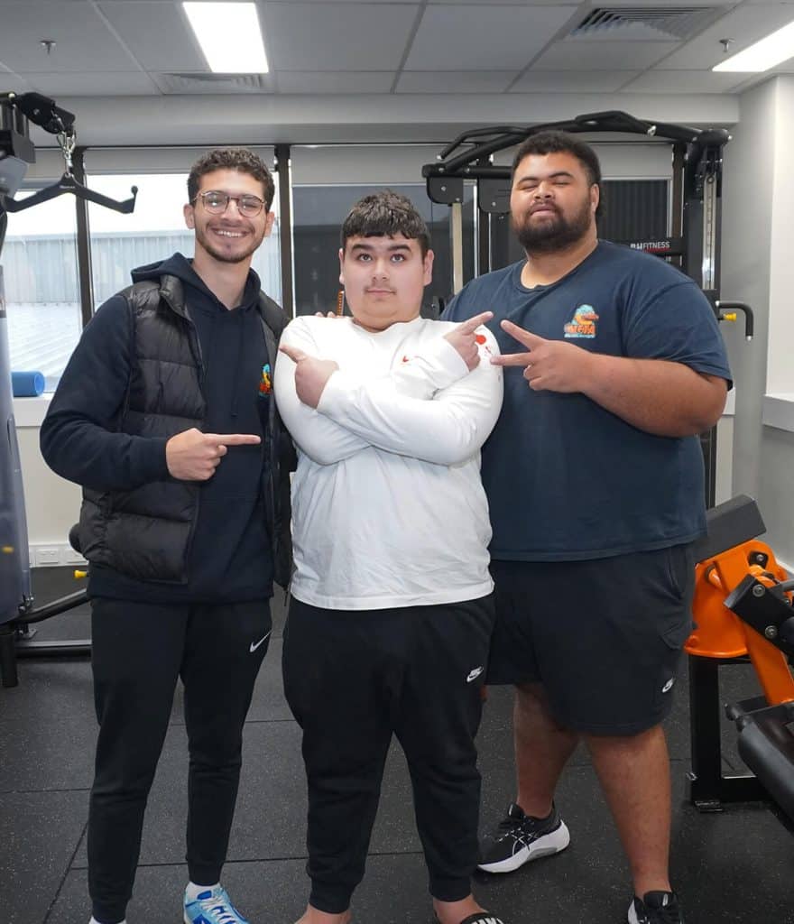 Group of three young men in sportswear standing together in a gym, promoting a healthy lifestyle.