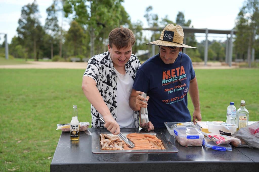 Two friends enjoying an outdoor barbecue, grilling sausages and vegetables in a park.