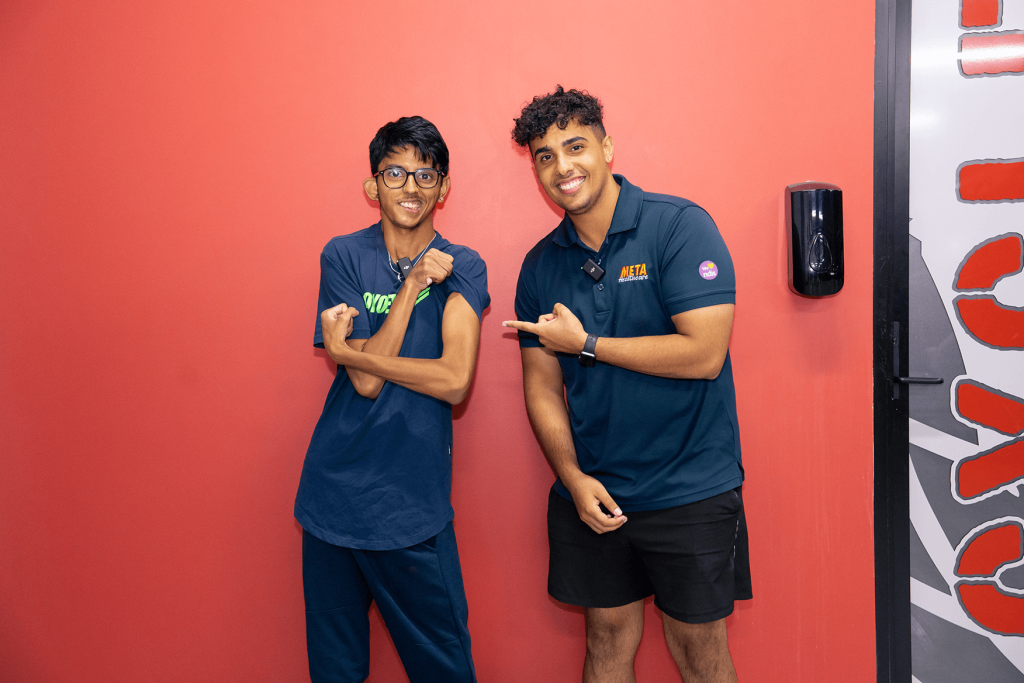 Two friends posing confidently in a fitness studio against a red wall.