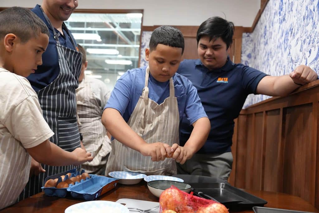 Children participating in a cooking class, cracking eggs into bowls.