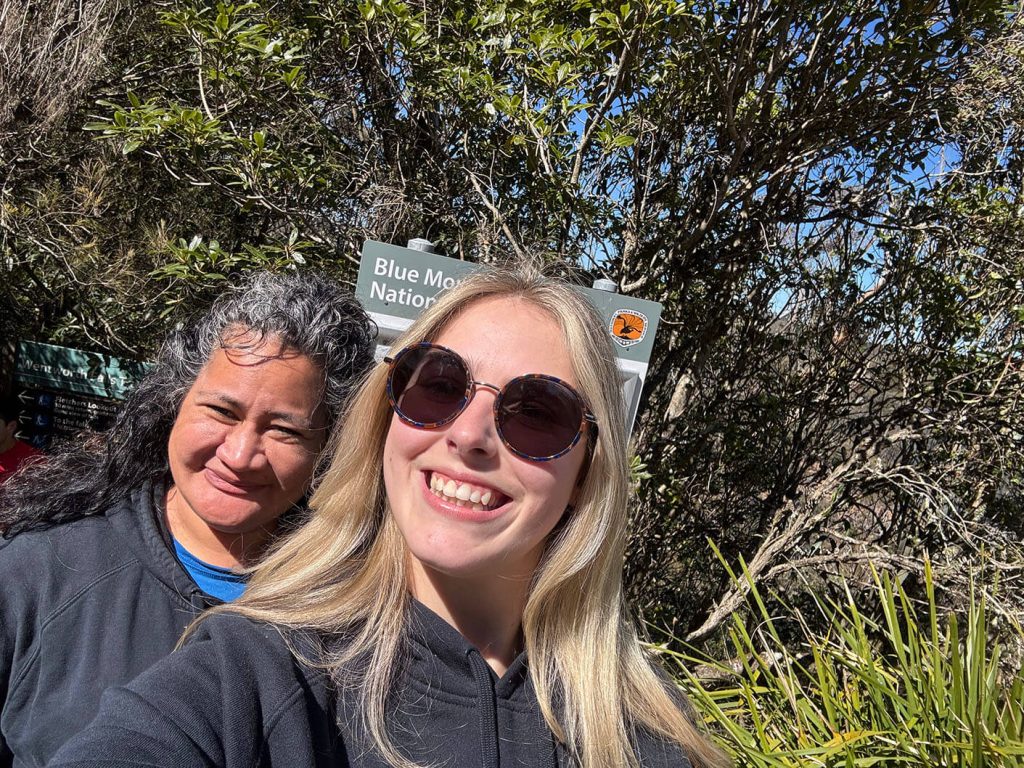 Two friends taking a selfie at Blue Mountains National Park with lush greenery in the background.