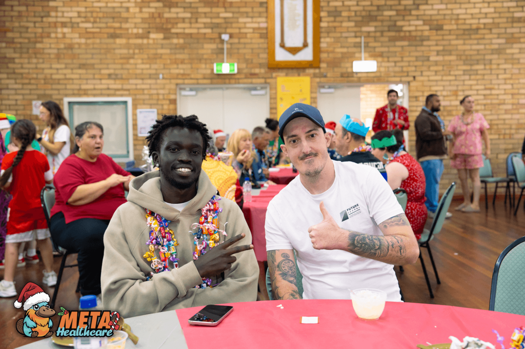 Two friends smiling at a community event with festive decorations.
