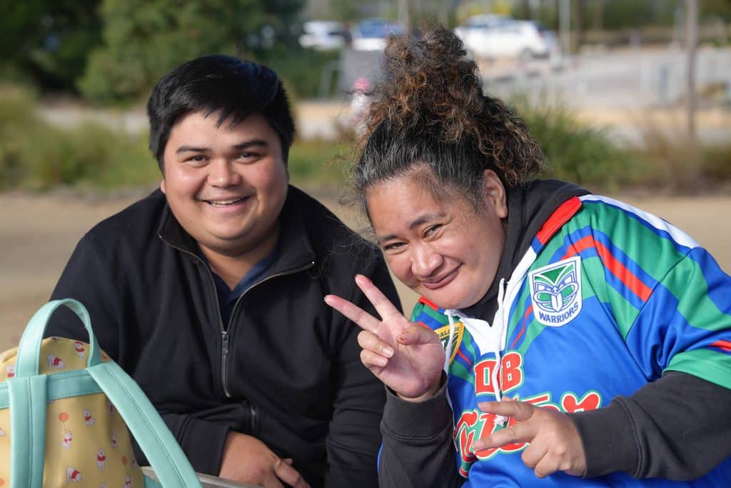 Two friends smiling together outdoors, one making a peace sign.