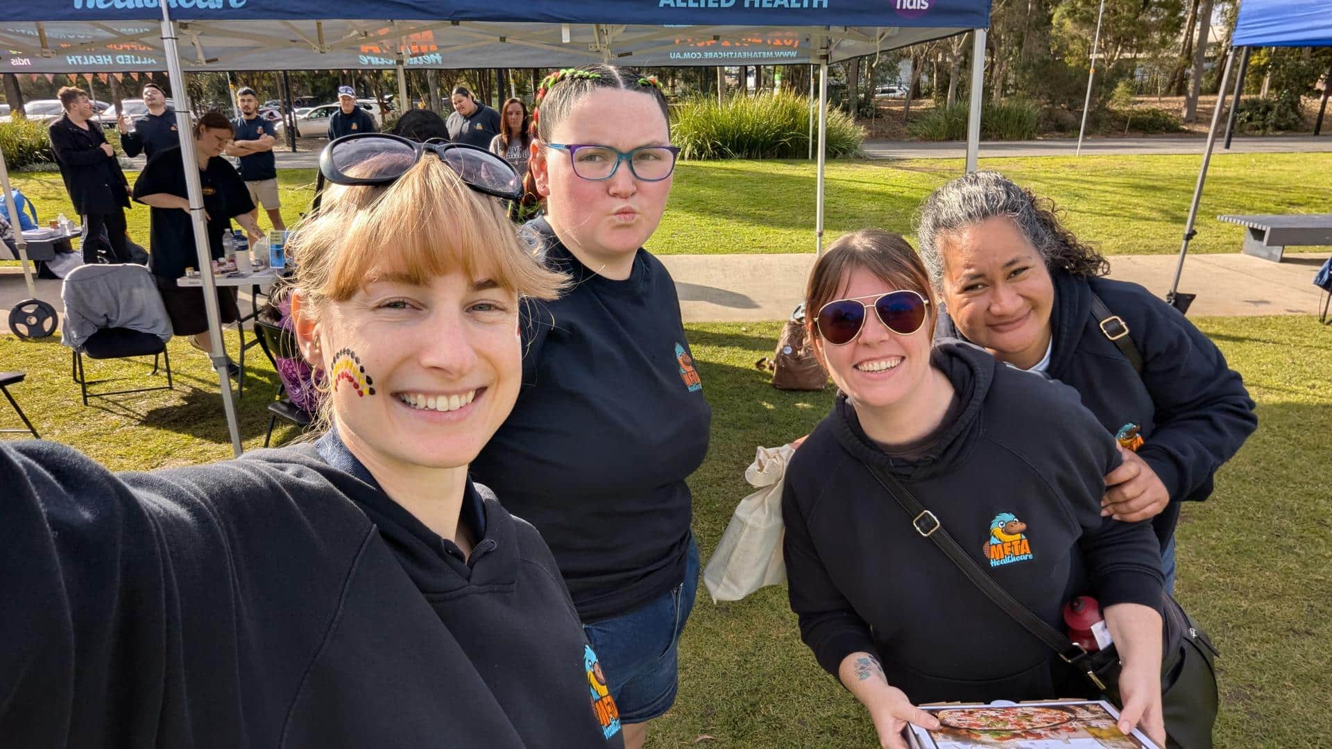 Group of friends smiling at a community event with colorful face paint.