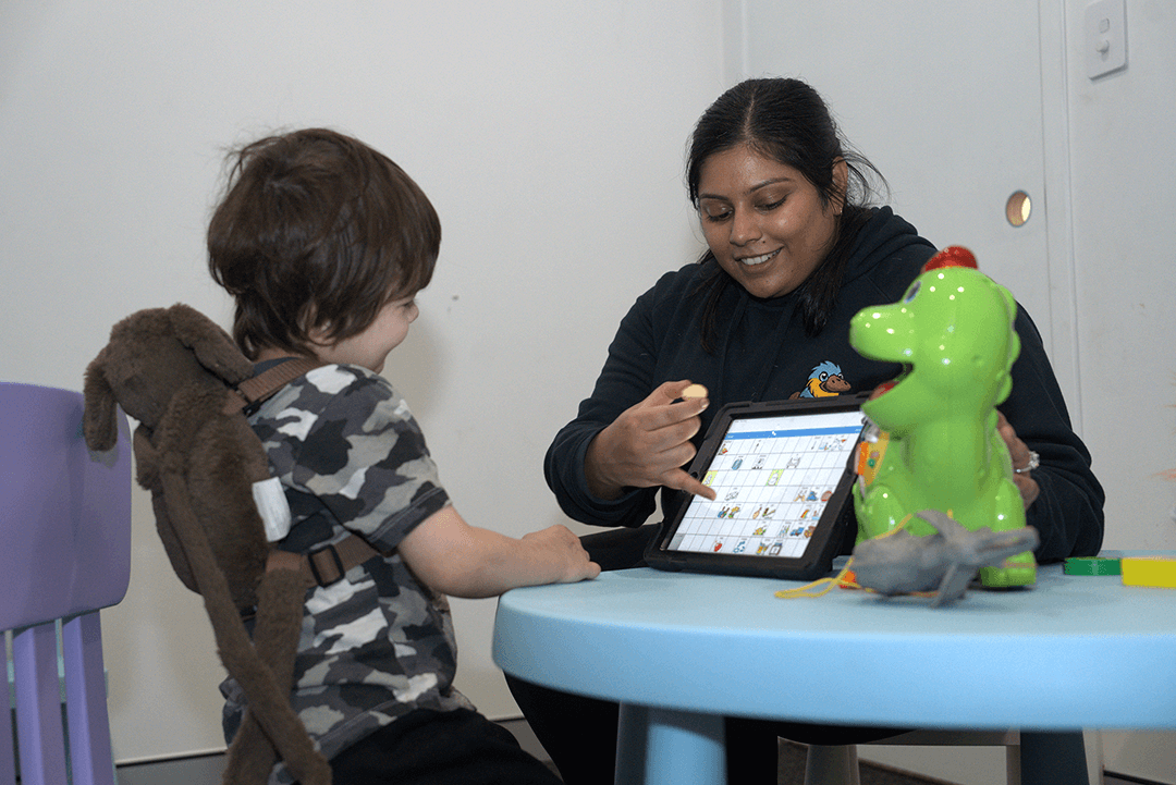 A child engaging with a teacher while using a tablet at a table.