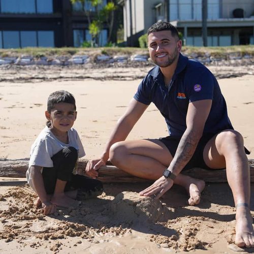 A man and a child playing in the sand at the beach on a sunny day.